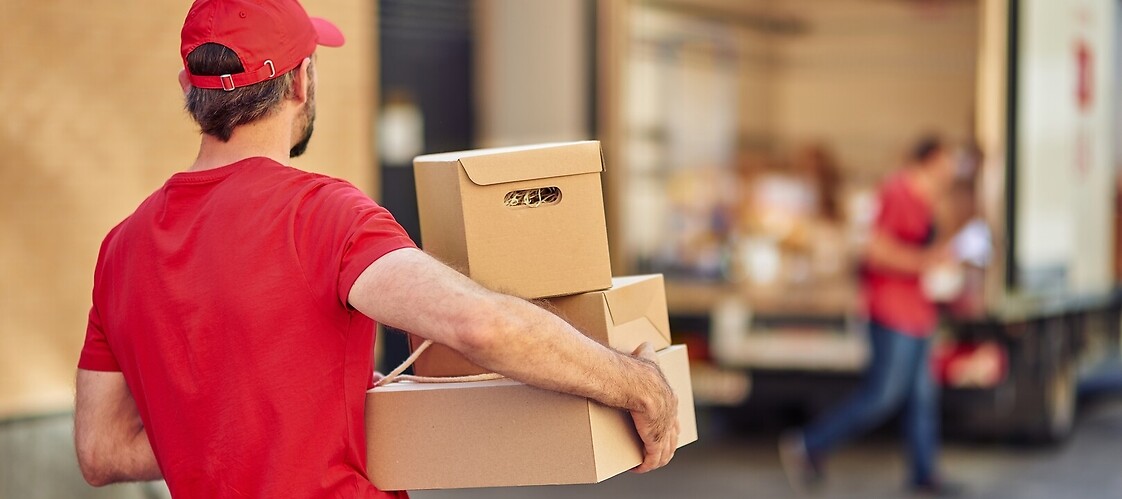 A man in a courier outfit carries parcels to a delivery van.