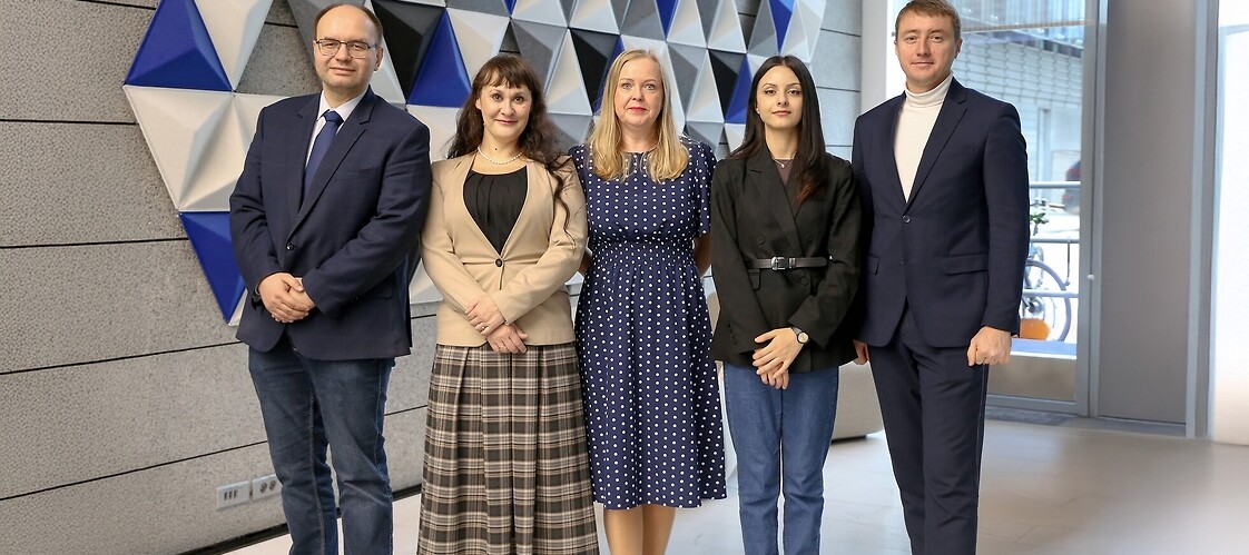 Five people in business attire pose for a photograph in an office space