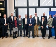 A group of people in business attire in an office space pose for a group photo