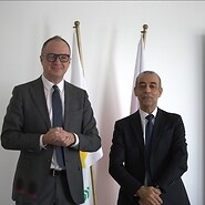 Two men in suits with the Cypriot and Polish flags in the background