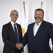 Two men in suits with the Cypriot and Polish flags in the background