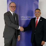 Two men in suits are shaking hands; a roll-up banner with the UKE logo is visible ...