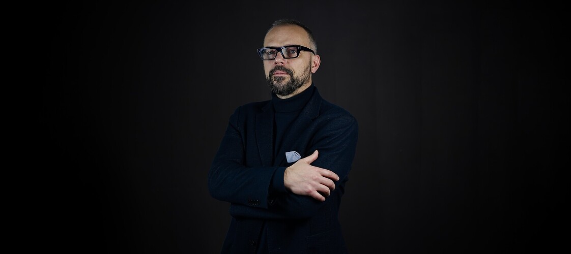 Męzczyzna w ciemnej marynarce i koszuli na ciemnym jednolitym tle