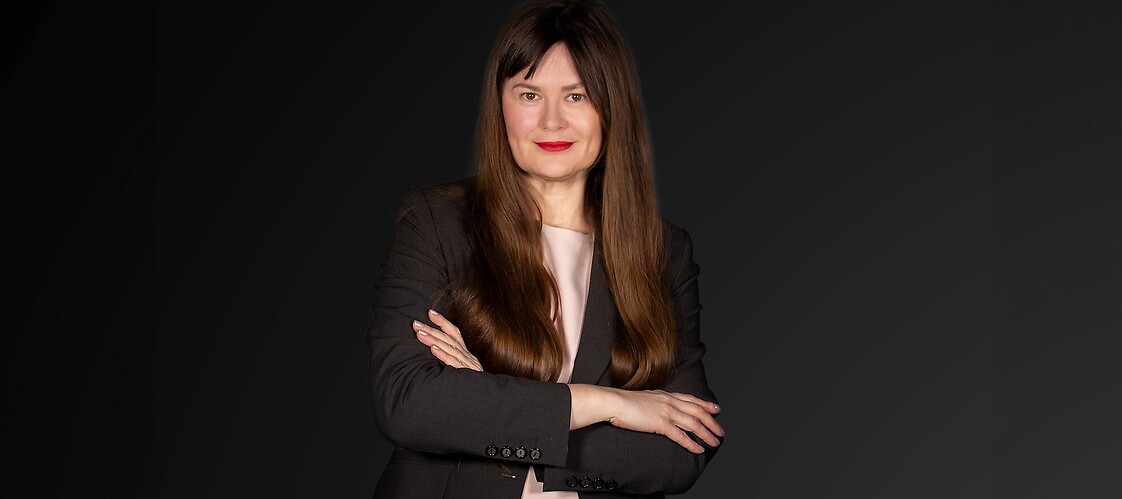 KObieta w ciemnym żakiecie i jasnej bluzce na ciemnym jednolitym tle