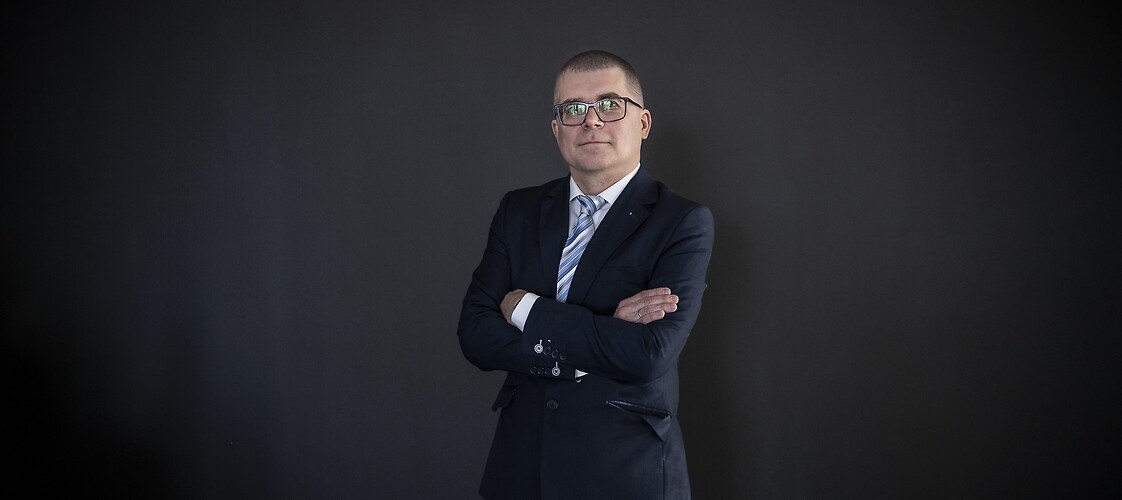 Mężczyzna w ciemnym garniturze i białej koszuli na ciemnym tle