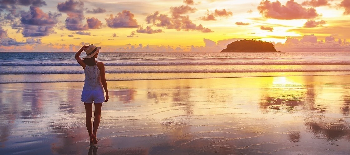 Kobieta stojąca tyłem na plaży na tle zachodzącego słońca