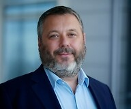 Mężczyzna w ciemnej marynarce i jasnej koszuli na tle biurowego wnętrza