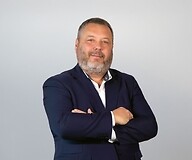 Mężczyzna w garniturze i białej koszuli, z założonymi rękami na białym tle