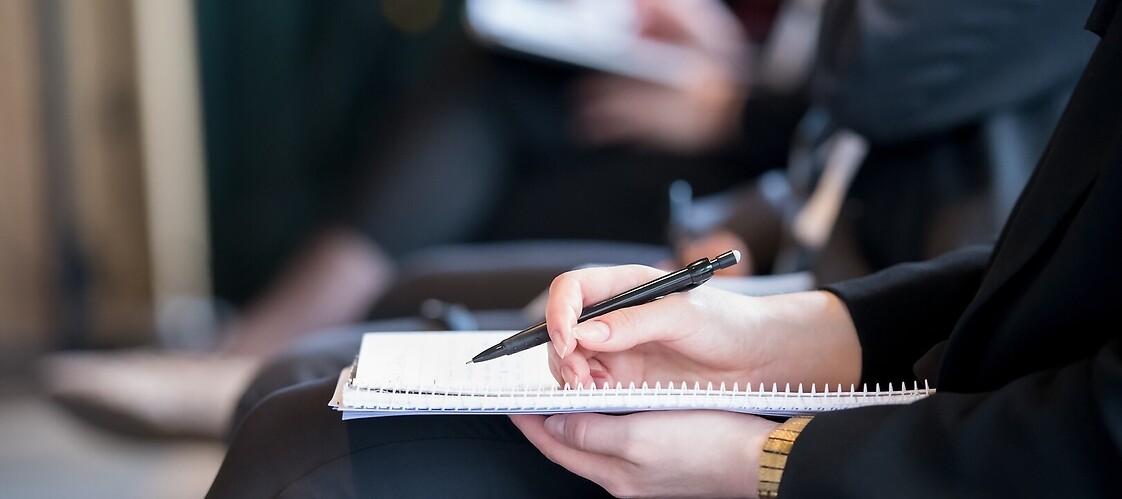 Dłoń na notatniku osoby siedzącej na spotkaniu