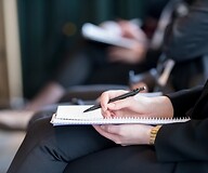 Dłoń na notatniku osoby siedzącej na spotkaniu