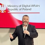 Męzczyzna w garniturze na tle godła i flagi RP oraz napisu Ministry of Digital ...