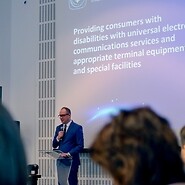 Męzczyzn w garniturze na tle prezentacji, na pierwszym planie głowy słuchaczy