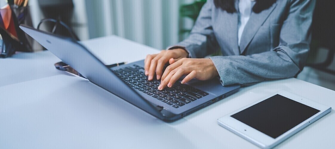 Dłonie na klawiaturze laptopa, obok telefon komórkowy