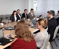 Grupa kilku osób w strojach biznjesowych po obu stronach stołu konferencyjnego