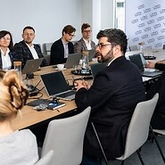Grupa kilku osób w strojach biznjesowych po obu stronach stołu konferencyjnego