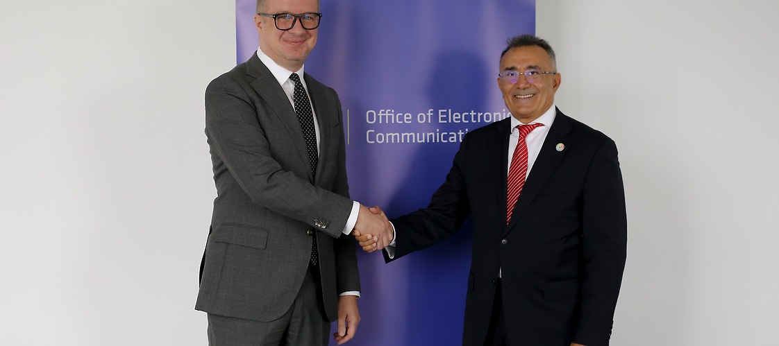 Dwóch mężczyzn w garniturach podaje sobie dłoń na tle rollupu z logotypem UKE