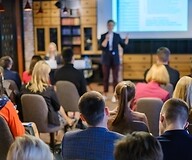 Griupa osób siedzi tyłem, patrząc na prowadzącego warsztaty