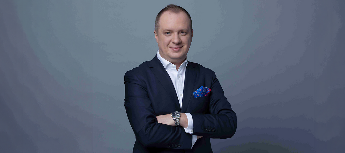 Mężczyzna w garniturze z założonymi rękami, na ciemnym jednolitym tle
